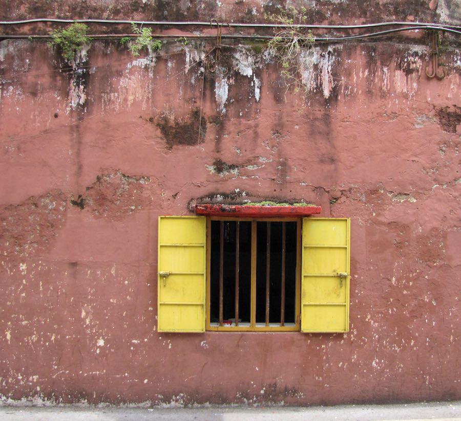 Window on a red wall with yellow shutters open